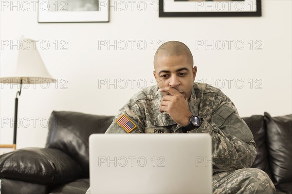 Mixed race soldier using laptop on living room sofa