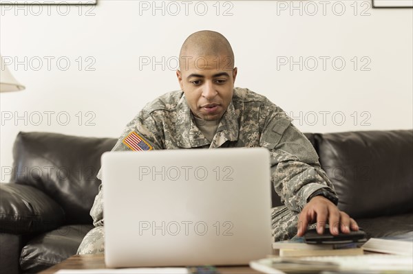Mixed race soldier using laptop on living room sofa