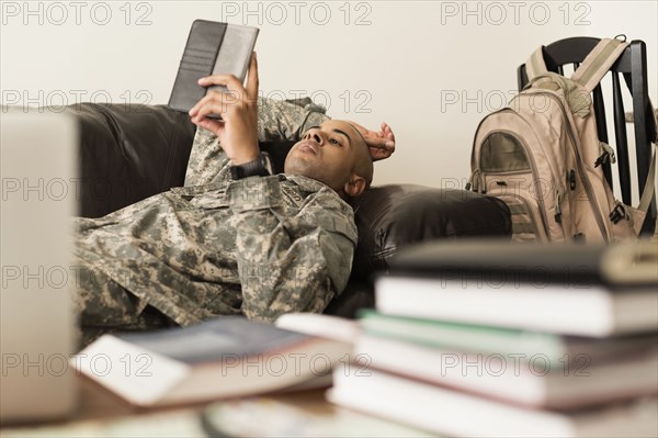 Mixed race soldier using digital tablet on sofa near books