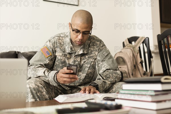 Mixed race soldier texting on cell phone and studying on sofa