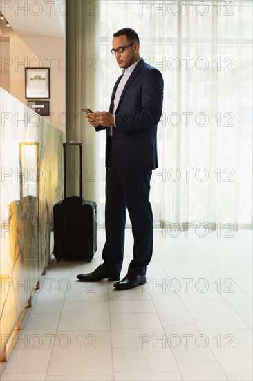 Hispanic businessman using cell phone at hotel front desk