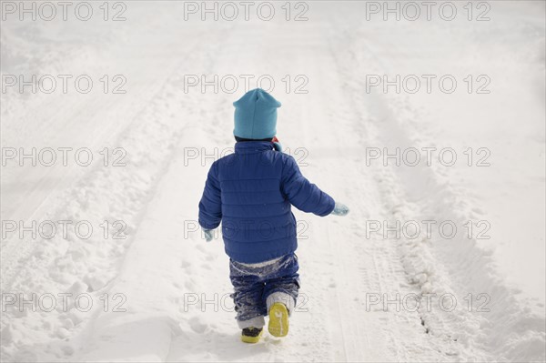 Caucasian boy walking in tire tracks in snow