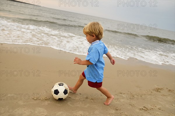 Caucasian boy playing with soccer ball on beach