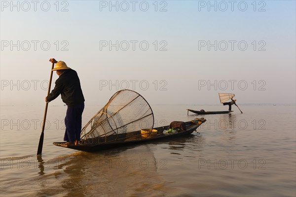 Asian fisherman rowing canoe on still lake