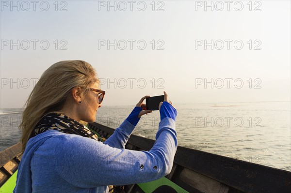 Caucasian woman photographing rural lake from canoe