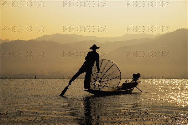 Asian fisherman rowing canoe on rural lake