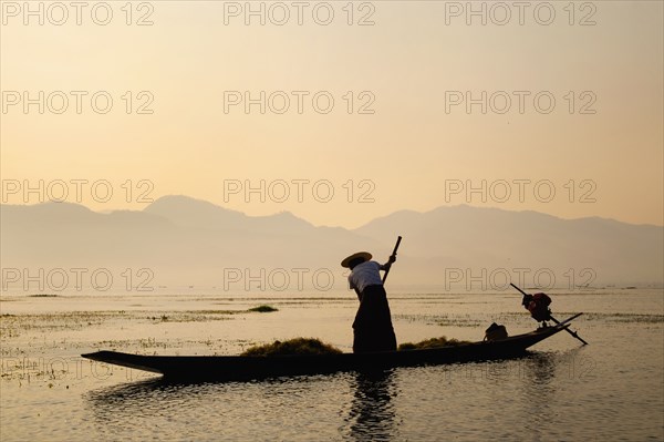 Asian fisherman rowing canoe on rural lake