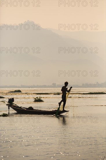 Asian fisherman rowing canoe on rural lake