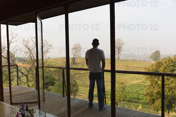 Asian man standing on balcony overlooking rural field