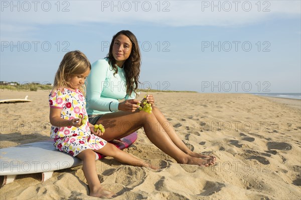 Mother and daughter eating grapes on beach