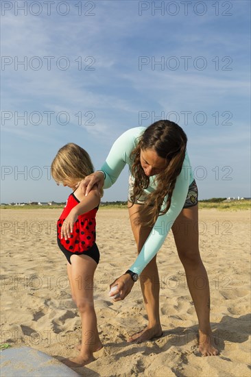 Mother spraying sunscreen on daughter at beach