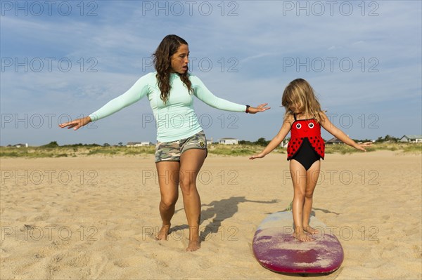 Mother teaching daughter to surf at beach