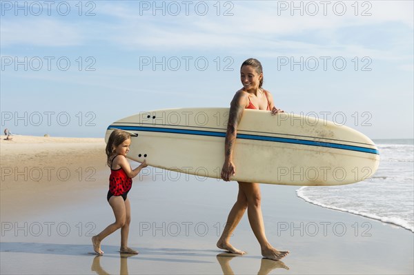 Mother and daughter carrying surfboard on beach