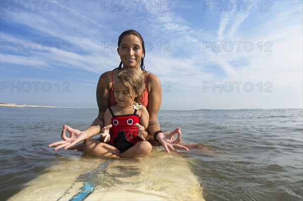 Mother and daughter meditating on surfboard