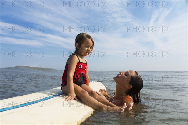 Mother teaching daughter to surf in ocean