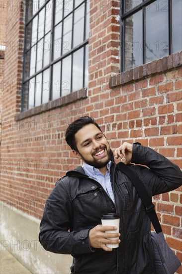 Hispanic man carrying bag and coffee cup in city