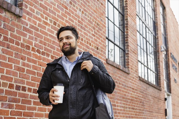 Hispanic man carrying bag and coffee cup in city