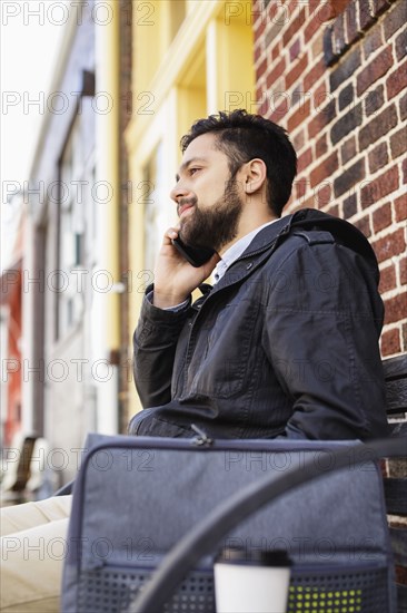 Hispanic man sitting on city bench using cell phone