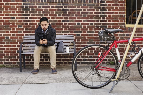 Hispanic man sitting on city bench using cell phone