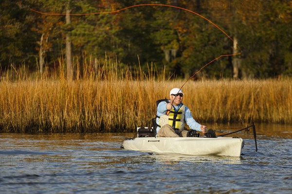 Caucasian man fly fishing in kayak on river