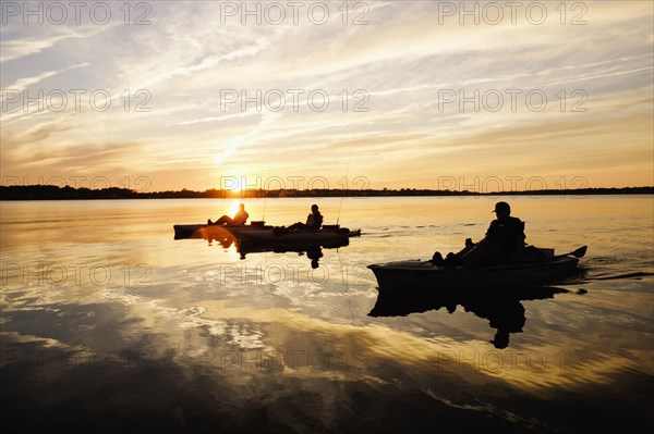 Silhouette of people fly fishing in kayaks on river