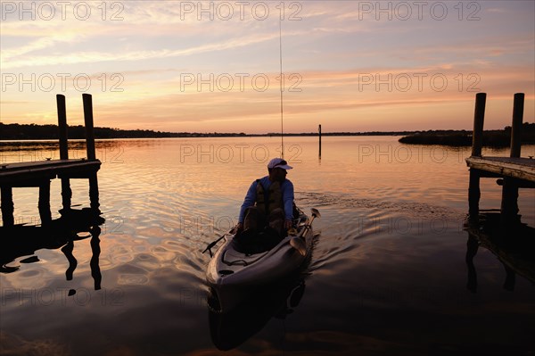 Caucasian man on kayak near dock at sunset