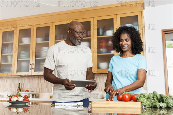 Black couple with digital tablet chopping tomatoes in kitchen