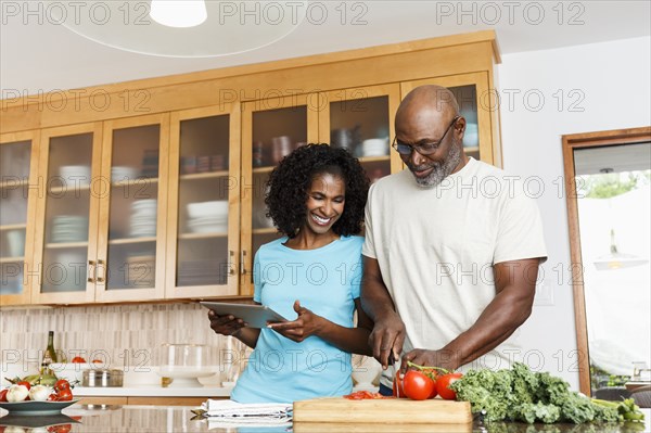 Black couple with digital tablet chopping tomatoes in kitchen