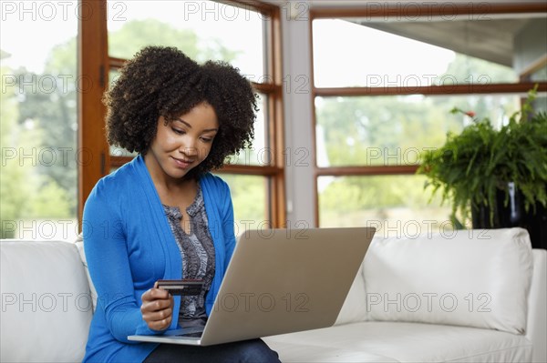 Black woman online shopping with credit card and laptop on sofa