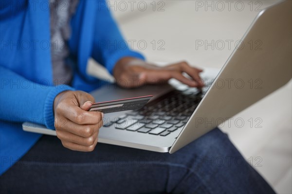 Black woman online shopping with credit card and laptop on sofa