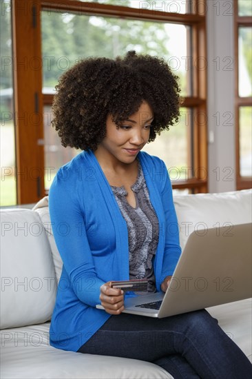 Black woman online shopping with credit card and laptop on sofa