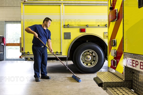 Chinese fireman sweeping floor near fire trucks