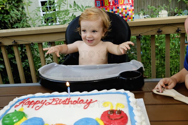 Caucasian baby boy in high chair near birthday cake