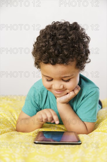 Smiling Mixed Race boy laying on bed using digital tablet