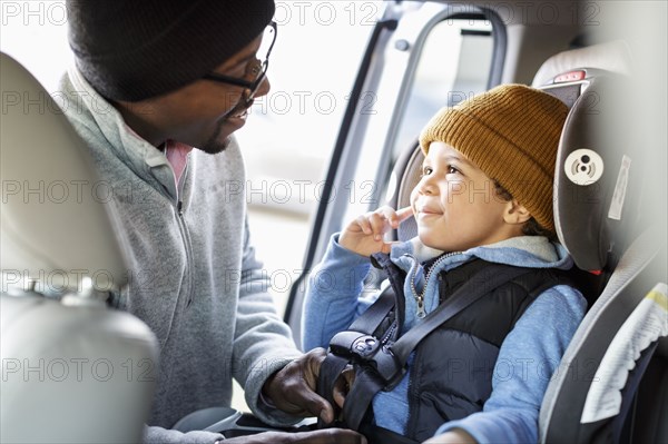 Father buckling son in car seat