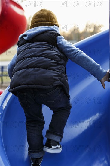 Mixed Race boy climbing on blue playground slide