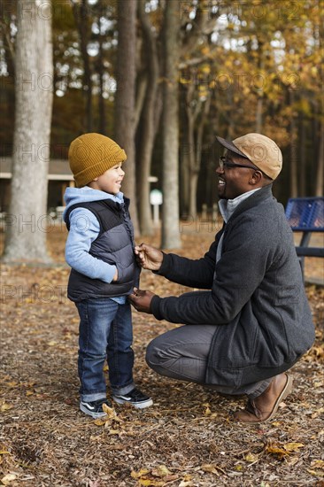 Father zipping vest for son in park