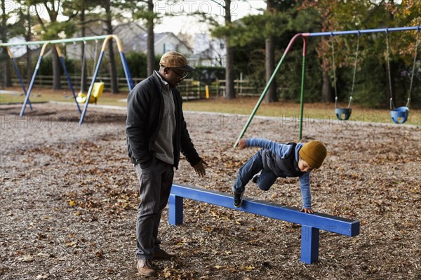 Father watching son jumping over playground beam