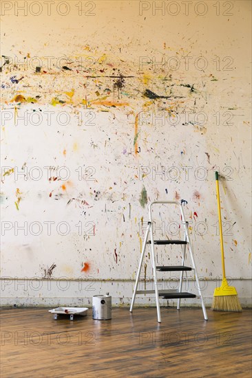 Paint splattered on wall near ladder and broom