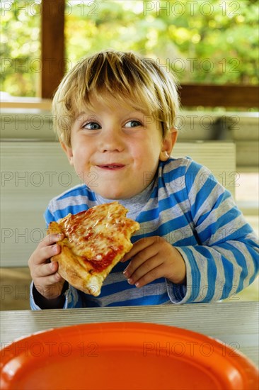 Playful Caucasian boy eating slice of pizza