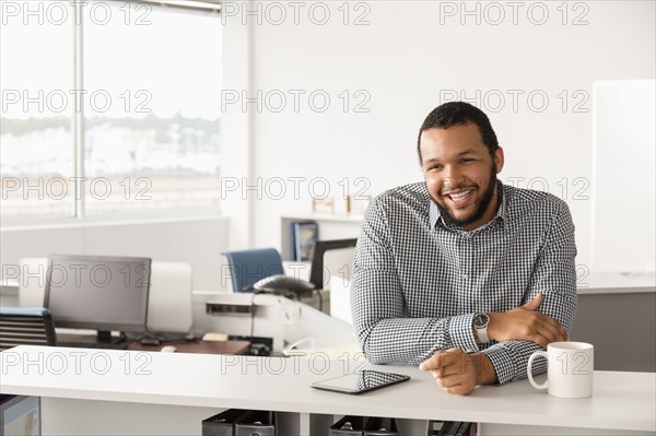 Smiling Mixed Race man leaning in office