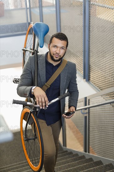 Mixed Race man climbing staircase carrying bicycle