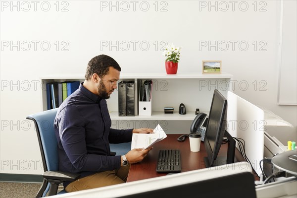 Mixed Race man reading paperwork near computer in office