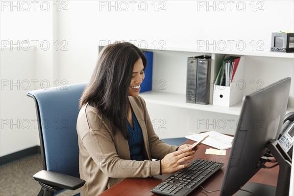 Pacific Islander texting on cell phone near computer in office
