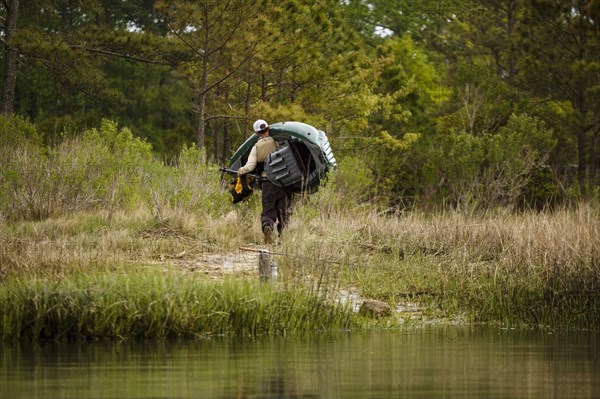 Caucasian man carrying fishing rod and kayak