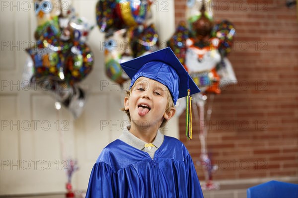 Caucasian boy wearing graduation robe sticking tongue out