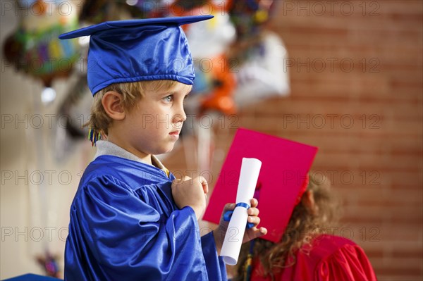 Caucasian boy wearing graduation robe holding diploma