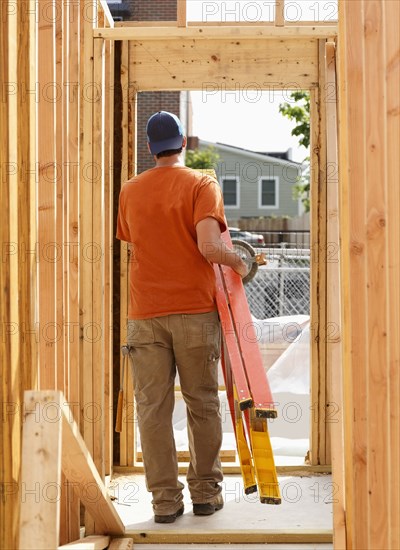 Caucasian man carrying ladder at construction site