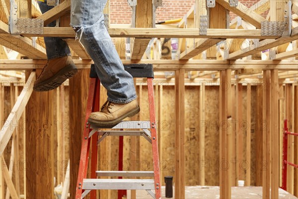 Legs of black man on ladder at construction site