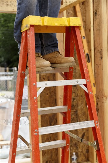 Legs of Caucasian man standing on ladder at construction site
